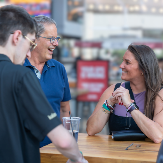 Three colleagues smile during a shared discussion in casual attire outside