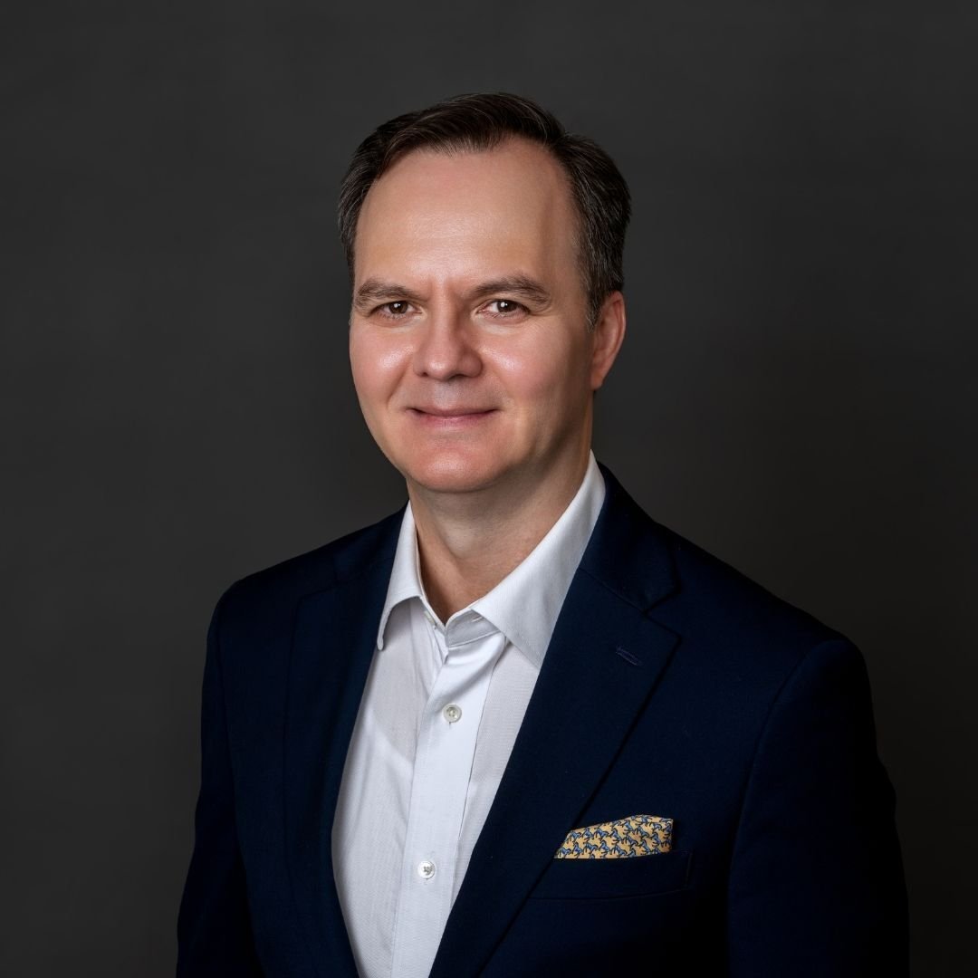 Carlos Salazar DBA, Chief AI Officer, smiles at the camera in a black suit against a dark background