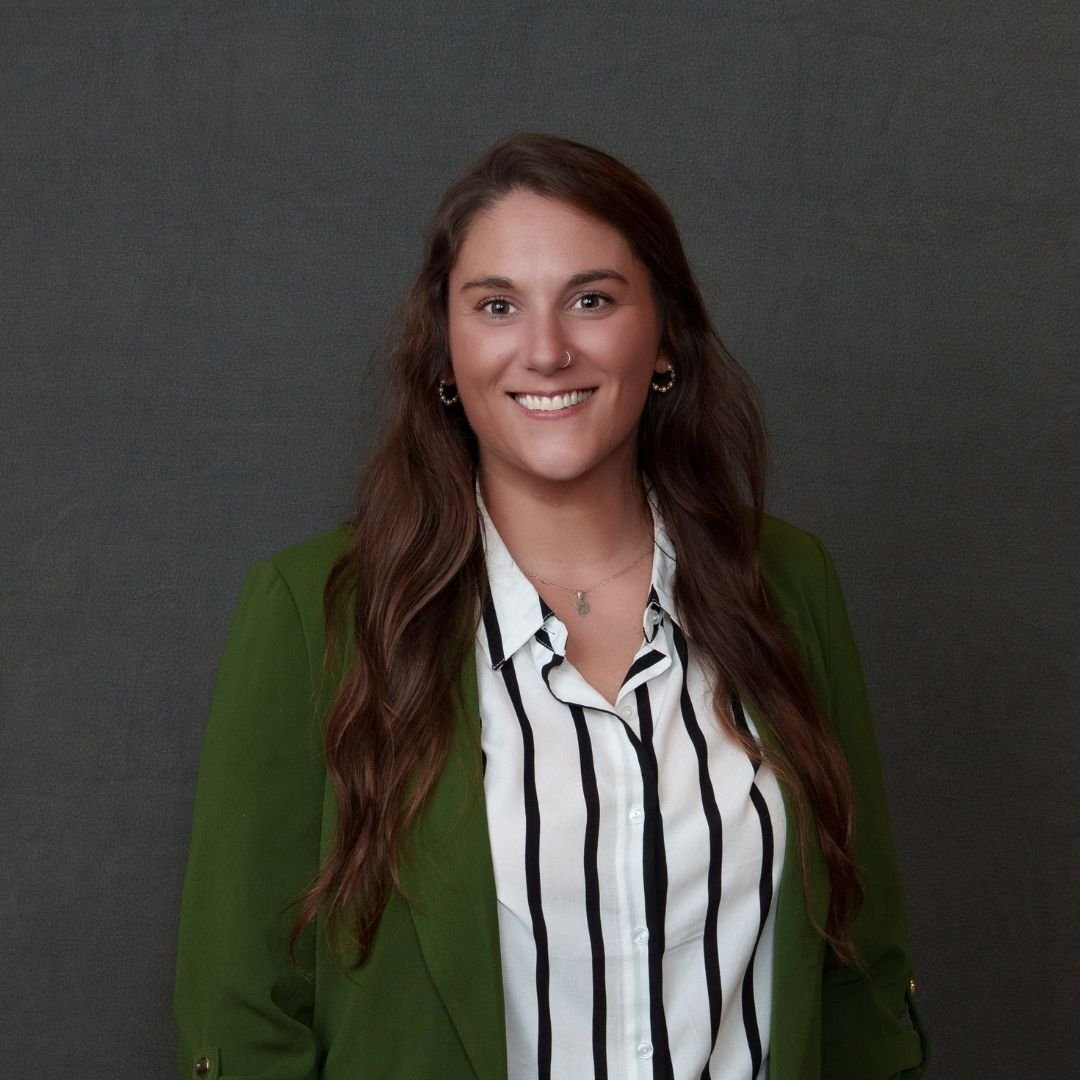 Jenni Yearta, Director of HR and Accounting, smiles at the camera in a green blazer against a dark background
