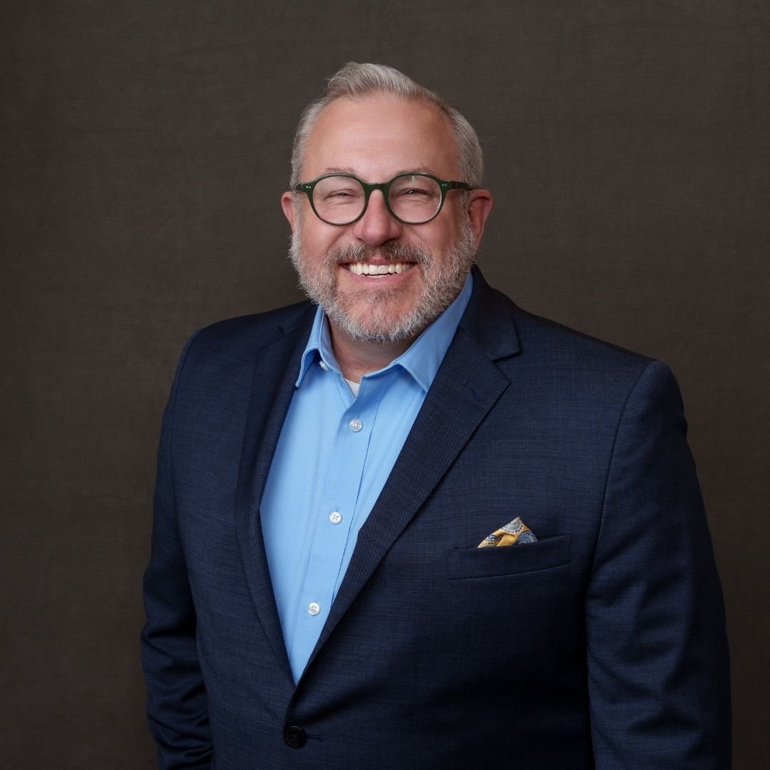 Chris Fredrickson, COO, smiles at the camera in a blue suit against a dark background