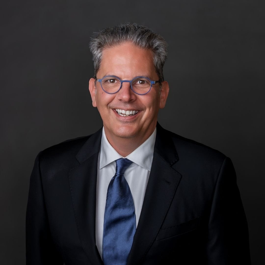 Jon Bohlke, Senior Partner, smiles at the camera in a black suit against a dark background