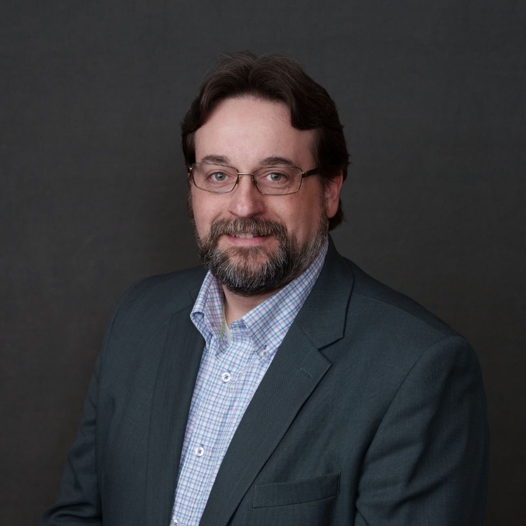 Jericho Simmons, CISO, smiles at the camera in a gray suit against a dark background
