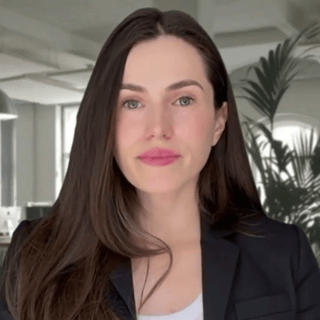 Alleria, an AI woman with dark brown hair, a brown blazer, and white T-shirt looks at the camera